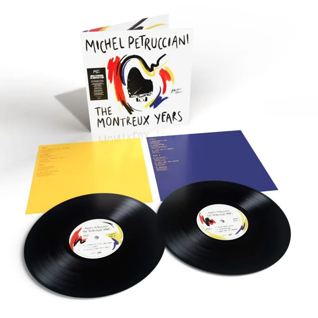 Deux disques noirs Michel Petrucciani, The Montreux Years, Double Vinyle avec des étiquettes colorées sont posés à côté de feuilles de tracklist jaunes et bleues. La pochette de l'album qui se trouve derrière eux présente un art abstrait audacieux en rouge, bleu, jaune et noir.