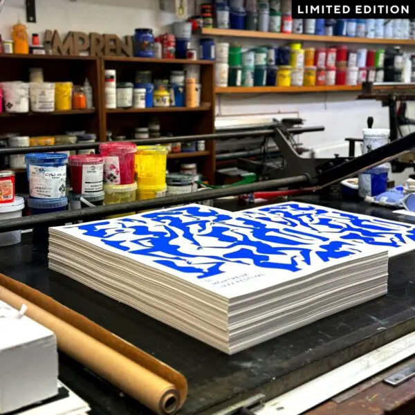 A stack of Poster Malika Favre, 2017, Limited Edition Blue prints with bold blue abstracts sits on a studio table surrounded by colorful ink cans. A "LIMITED EDITION" label is featured in the top right corner.