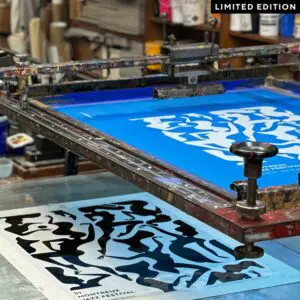 A screen printing press applies blue ink to paper, creating bold abstract shapes in the style of "Poster Malika Favre, 2017, Limited Edition Blue." The workspace is filled with art supplies, with LIMITED EDITION in the top right corner.