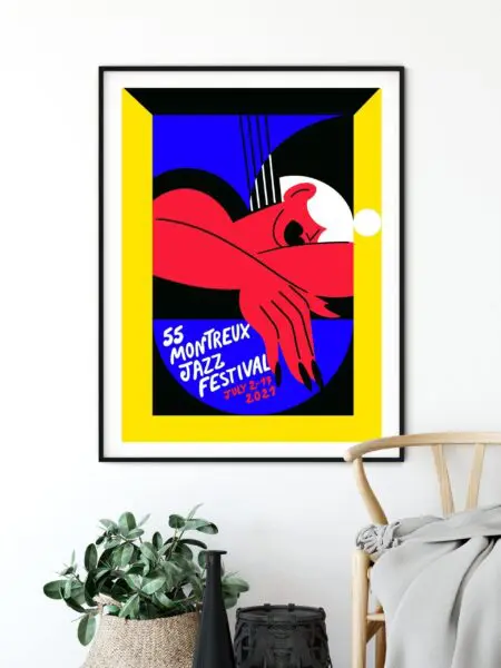 Poster Marylou Faure, 2021 displays abstract red arms, hands, guitar, and bold black, blue, yellow, and white tones with handwritten event details. The framed poster is shown hanging above a chair and plant.