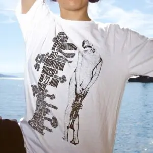 A person wearing a T-Shirt Eric Wondergem, 1969, with black text and graphics for the 1969 Montreux Jazz Festival, stands outdoors by a body of water on a sunny day.