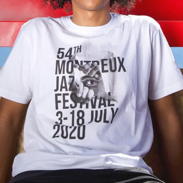 Someone wears the T-Shirt JR, 2020, Montreux Jazz edition, which showcases bold black text—54th Montreux Jazz Festival 3-18 July 2020—and an eye graphic peering through torn paper.