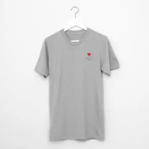A gray short-sleeve T-shirt hangs on a white hanger against a white wall, featuring heart embroidery and "I love you" text on the chest—a subtle tribute to Montreux style from the T-Shirt Heart Embroidery, Montreux Jazz Festival collection.