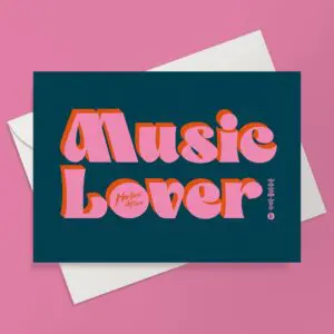 The Music Lover Card features bold, retro pink and orange text on a dark blue background—perfect for celebrating a music festival. Shown on a white envelope against a pink surface.