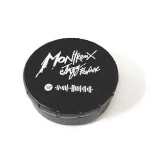 L'Ecobox Montreux Jazz Festival est une pochette ronde noire avec "Montreux Jazz Festival" en écriture blanche, un logo Spotify et un code à scanner sur le couvercle, sur fond blanc.