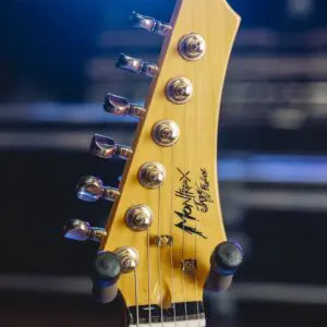 Close-up of a light-colored electric guitar headstock from the Atlanta, Guitar Collection, Limited Series, featuring six tuning pegs and Monterey Custom Shop logo, captured at Montreux Jazz Guitar Atlanta with bright stage light and blurred background.