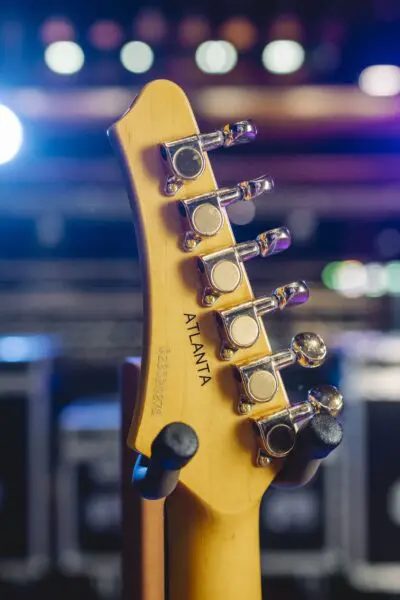 Close-up of the back of a Limited Series Atlanta Guitar Collection headstock with tuning pegs and "ATLANTA" engraved, set against blurred stage lights—evoking Montreux Jazz Guitar style in an Atlanta-inspired design.