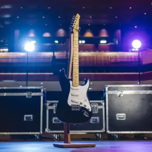 The Detroit Guitar Collection Limited Series features a black electric guitar on a wooden stand, showcased under stage lights with black equipment cases and a concert hall backdrop, capturing the vibrant Montreux Jazz atmosphere.
