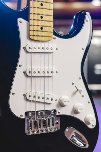 Close-up of the Detroit Guitar Collection, Limited Series electric guitar featuring a white pickguard, three single-coil pickups, volume and tone knobs, bridge, and maple neck; its shiny black body channels a classic vibe.