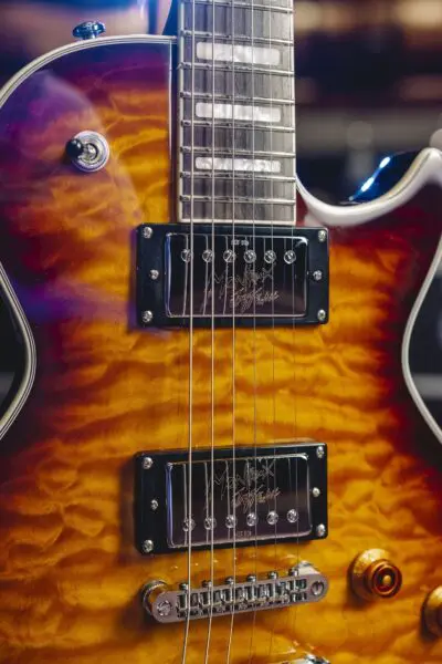 Gros plan d'une guitare électrique avec une finition sunburst ambre matelassée, un accastillage chromé, deux micros humbucker et un seul bouton de contrôle ambre visible.