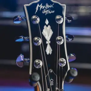 Gros plan d'une tête de guitare avec des chevilles d'accordage, avec un motif incrusté et le logo "Montreux Jazz Festival" dans la partie supérieure. L'arrière-plan est flou et éclairé en bleu et en violet.