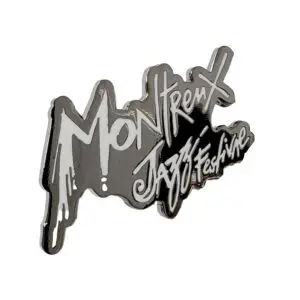 L'épingle Montreux Jazz Festival présente un lettrage stylisé blanc et argenté de type graffiti sur un fond métallique réfléchissant.