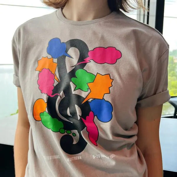 A person wearing the T-Shirt Shigeo Fukuda, 1985—a light gray tee with colorful comic-style speech bubbles, a bold black treble clef, and Montreux festival text at the bottom.