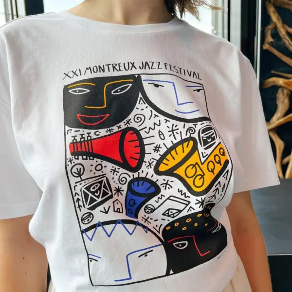 A person wearing a T-Shirt François Boisrond, 1987, featuring colorful abstract faces, musical instruments, patterns, and the text “XXI Montreux Jazz Festival” above the design.