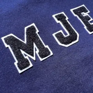 Gros plan sur un tissu bleu marine sur lequel sont cousues des lettres noires et blanches texturées de style varsitaire, M et J.