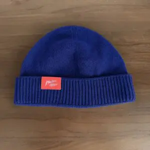 A royal blue knit beanie named "Blue Hat, Montreux Jazz Festival" features a folded brim and a red rectangular patch with white cursive text, displayed on a wooden surface.