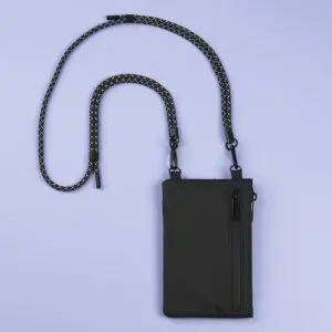 A compact black Festival Bag, Lakeside, with a zippered front pocket and detachable black-and-white rope strap, shown on a light purple background.