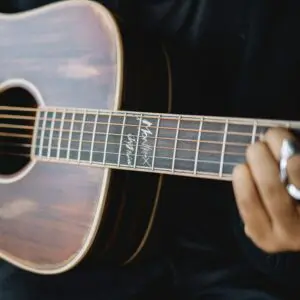 A close-up of a person playing the Miami Electro Acoustic Guitar, Limited Serie shows the player's hand forming a chord on the fretboard, which features signature markings and a dark wood finish.