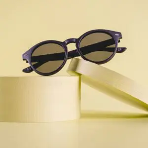 A pair of Fly Bruxelles Matte Black Glasses rests atop two yellow cylindrical pedestals—one tilted—against a matching yellow background.