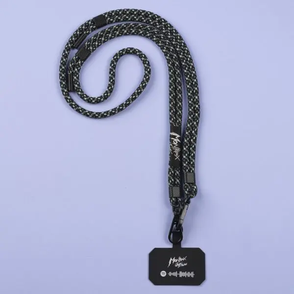 The Mobile Strap, Lakeside—a black and gray patterned lanyard—holds a black card with white text, a signature graphic, and a Spotify code, shown on a light purple surface at Montreux. Perfect as a festival mobile strap.
