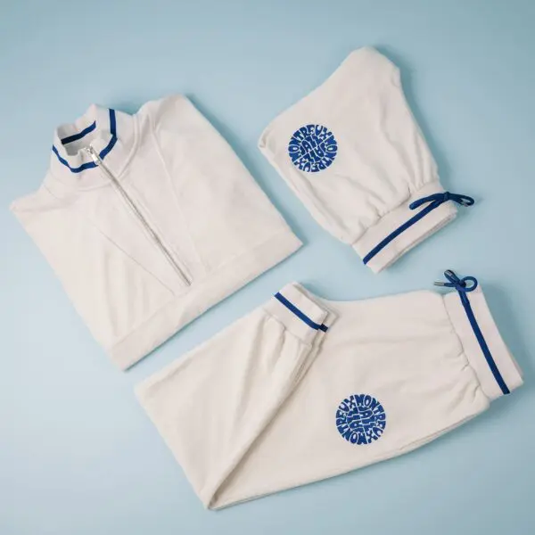 The Sweat Unisex Terry Cloth Zip-Up Trucker Collar Vintage set is a white three-piece tracksuit with blue trim and the Monkeywork logo, including a jacket and two pants, displayed on a light blue background.