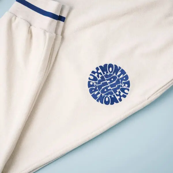 Trousers Terry Cloth, Vintage: Off-white sweatpants with blue-striped waistband and bold MONTRÉAL graphic on the leg, laid flat on a light blue surface.