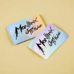 Deux cartes Sticker holographique Montreux Jazz Festival avec une finition brillante, irisée par l'arc-en-ciel et une écriture noire audacieuse sont placées sur une surface beige clair.