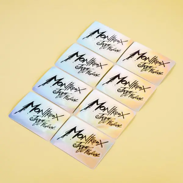 Nine pastel-colored cards are arranged in a grid on a light yellow surface, each showcasing the Holographic Sticker Montreux Jazz Festival with bold artistic lettering and a stylized mountain graphic.