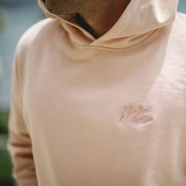 A person wearing the Sweatshirt Montreux Jazz embroidered, Peach, is pictured from the neck down with a blurred background.