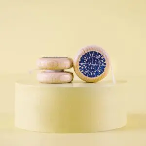 Three Vintage Yoyo Montreux Jazz wooden yo-yos with blue text are displayed on a round yellow pedestal against a yellow background. One yo-yo stands upright to showcase its design, while the other two are lying flat.