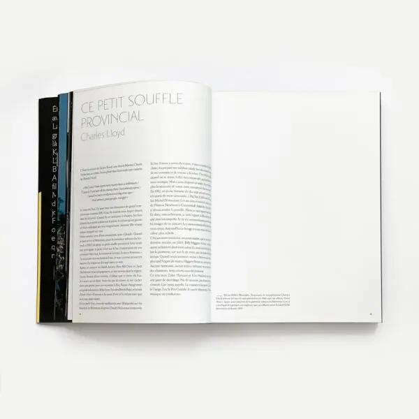 An open book titled "50 Summers Of Music" shows a section called CE PETIT SOUFFLE PROVINCIAL by Charles Lloyd on the left page, with text below. The right page is mostly blank, and several other books are partially visible underneath.