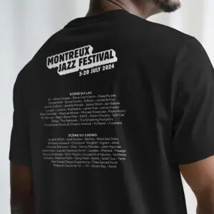 A person wearing a black T-Shirt Lineup 2024, Limited Edition, featuring Montreux Jazz Festival dates and a list of Scène du Lac and Scène du Casino artists, all printed in white on the back.