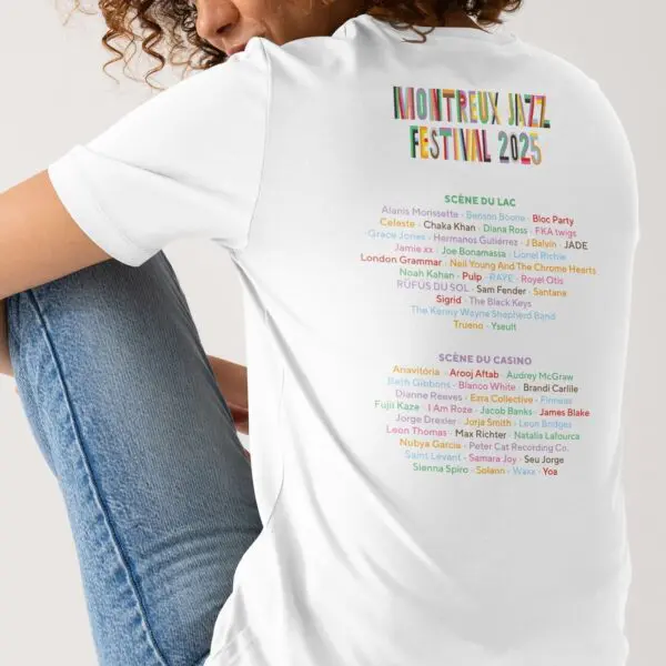 A person is seated, showing only their back and part of their curly hair, wearing the Limited Edition T-Shirt Lineup 2025 with Montreux Jazz Festival 2025 and vibrant performer names printed on the back.
