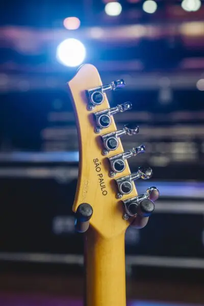 Close-up of the São Paulo guitar headstock from the Guitar Collection Limited Series, showing tuning pegs, SÃO PAULO engraved on the wood, and a bright stage light in the blurred background.