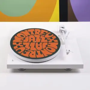 La Feutrine Vinyle Vintage est une platine blanche avec un plateau coloré présentant le dessin abstrait de Lakwena et le texte rétro orange "Montreux Jazz" sur un fond vibrant.