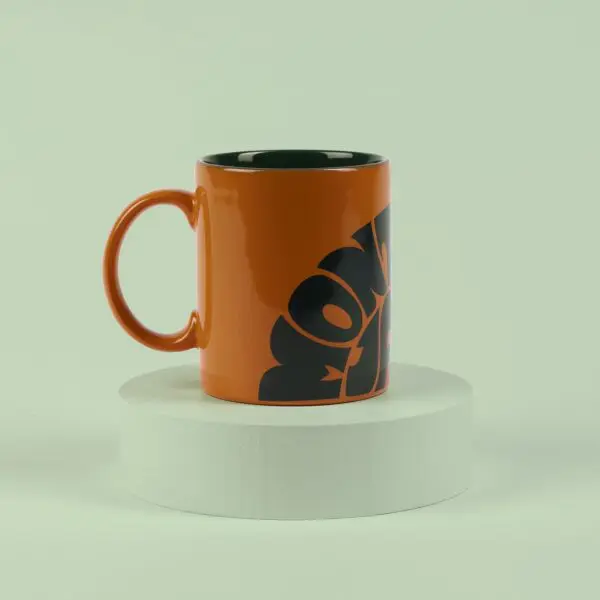 The Mug Vintage Orange, featuring a black abstract design, is displayed on a round white pedestal with a pale green background, capturing the lively spirit of Montreux Jazz.